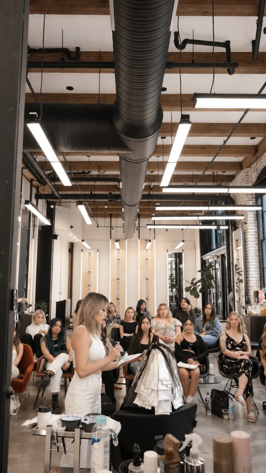 A full class of stylists gathered around Jennifer Slim during a hands-on salon education event.